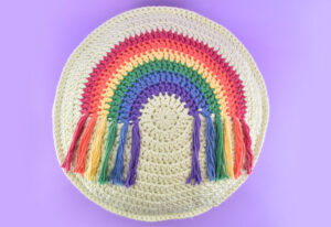 Looking for a fun, colorful, and fringed DIY addition to your decor? Get the free pattern and hook up this round crochet rainbow pillow!