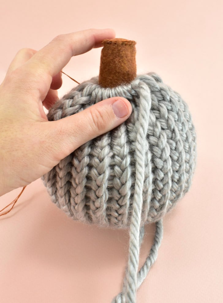 Begin pulling the tail at the top of the pumpkin to begin closing the hole. Place the stem into the hole and pull the yarn tightly for a secure fit. It might be necessary to finagle the pleats around the stem for a neat look.