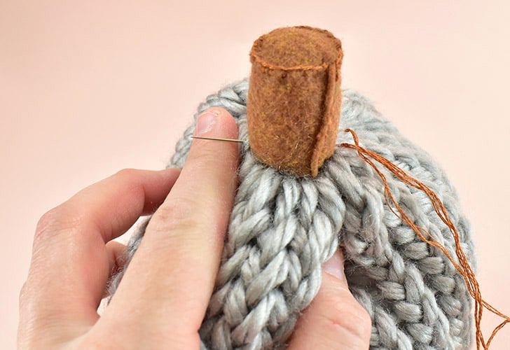 Re-thread your embroidery needle with the tail from your stem. Use it to stitch through the yarn into the stem and out of the other side to secure the stem to the pumpkin. 