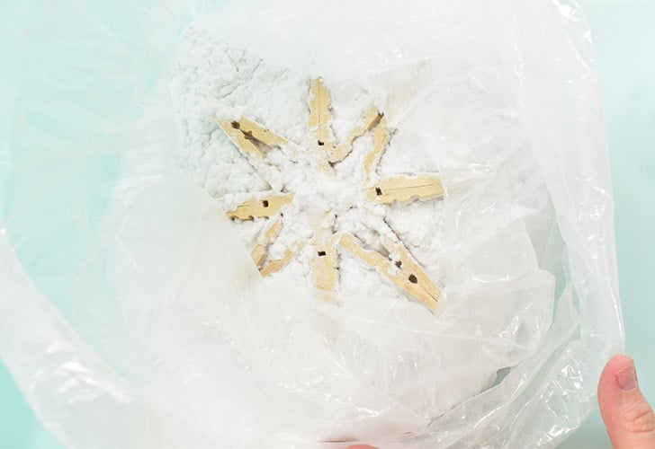 Place the snowflake with the still wet Mod Podge into a bag of flock. If you have leftover from other projects you might want to just toss your snowflakes in the bag the material came in. If you have other projects in mind, you might want to transfer some flock to a large zipper bag. Carefully move the snowflake around in the flock until all of the adhesive is covered. Lay the snowflake newly flocked side up.