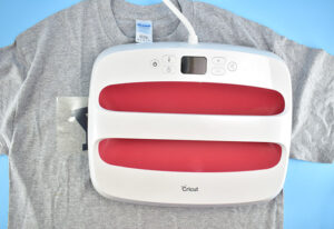 With your design in place, put your Teflon sheet on top of the carrier sheet. Place your heated press or iron onto the design