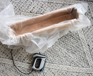 Line the inside with a plastic painter's tarp or roofing paper. Fold the material in at the corners so that there are no gaps between the material and the walls of the planter.