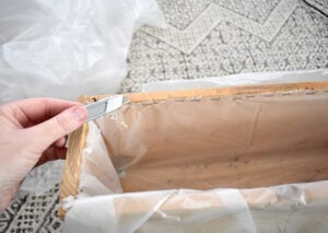 Using a staple gun, tack the material into place a half an inch below the edge of the planter. Use a sharp utility knife and carefully trim away the excess.