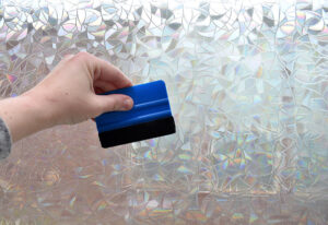Working from the the center outward, like a sunburst, use your felt covered squeegee to apply the film to the window and remove any air bubbles or water.