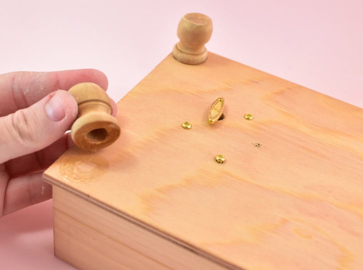 While still upside down, apply a strong adhesive to the open end of small wooden candle cups. Place them adhesive side down on the four corners of the box to act as feet and give some room for the handle to turn as the music plays. Remove the cups and give the glue a few seconds to become tacky. Replace the feet and allow the glue time to dry, several hours is good but overnight is best.