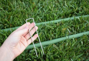 To anchor in the grass you'll need Landscaping Staples. They are inexpensive and can be hacked for a lot of garden use making them reusable. Simply push the staples into the ground around the pipes. If your ground is hard a mallet or hammer will help you set them firmly in place. The more staples you use the more sturdy the candy chute will be.