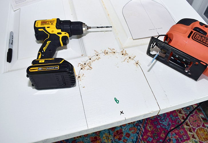 Drill several holes inside the marked arch. Take care to hold the drill nice and straight so that your holes on the backside stay within the arch's shape. Cut the arch shape out with a jigsaw, again holding the tool straight so as to cut within the arch's shape for both sides of the door.