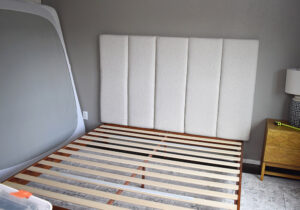 Laying your headboard upholstered side down, attach D-Rings to the back of your headboard to hang it on the wall. Place them about 3 inches down, one on the first and last panels and another in the middle if the headboard is larger. Measure out the placement of your hooks and place monkey hooks in the wall at those locations where you will hang your headboard.