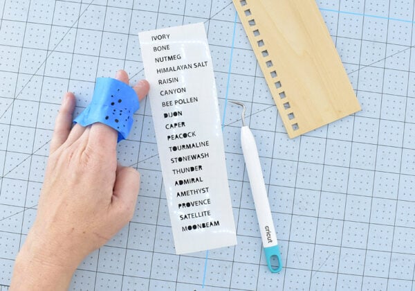 Using the Cricut Design Space File, swap out the "Yarn Color" line for the name of your yarn. If using the SVG cut files you can still head over to the design space file to get the proper spacing. If you're using another cutting program, or if you just prefer to do it yourself, type up the names and play with the line spacing until the names will sit next to the boxes on your cards. Weed away the excess vinyl making sure to get the little bits inside of letters like B. Apply a piece of transfer tape on top of all of the vinyl names. Use a scraper to burnish the vinyl onto the transfer tape. Slowly peel the tape upward. Lay the tape back down and apply more pressure to any letters that do not come away with the tape.