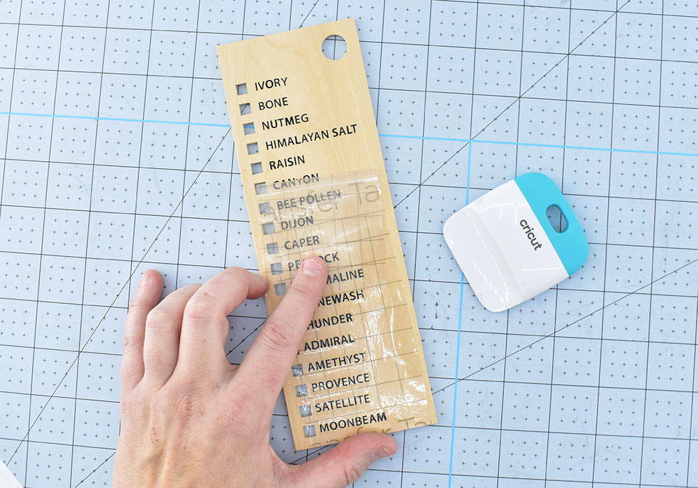 Carefully place the names next to each of the squares like you see above. Use your scraper to rub pressure over the transfer tape, transferring the vinyl onto the wood. Slowly peel away the transfer tape, laying it back down to apply more pressure to any letters that aren't sticking.