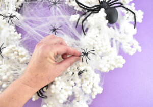 Stick your smallest spiders in the web in the center of the wreath and around. Just place the legs inside of the web and give it a little wiggle. The spider should hold on pretty well, but add a drop of hot glue if you'd like them to be more secure.