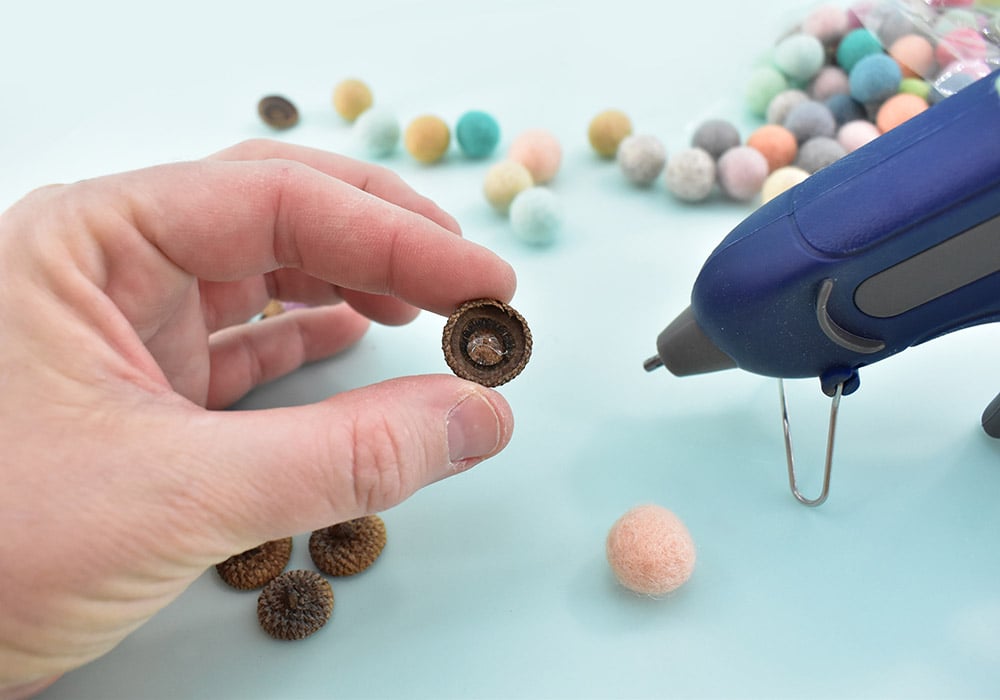 Not all of your felt balls will be exactly the same size and neither will your acorn hats. Before committing to anything with glue, test to find a ball and cap that fit together well. Apply a nice dab of glue inside of the acorn hat.