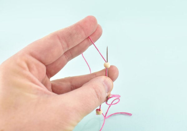 Run your line through an embroidery needle. Push the needle and string through the bead. Come back around and push the needle through one more time in the same direction. Hold onto the tail of the thread and pull the needle away from the bead. As you pull the string will form a loop around the bead.