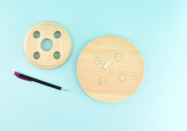 Place the larger wood round beveled side down. Place the top piece onto the bottom and center the larger holes around the predrilled tiny holes you previously created. Using a pencil trace the holes onto the bottom of that round. Drill each hole with your 3/4" spade wood bit.