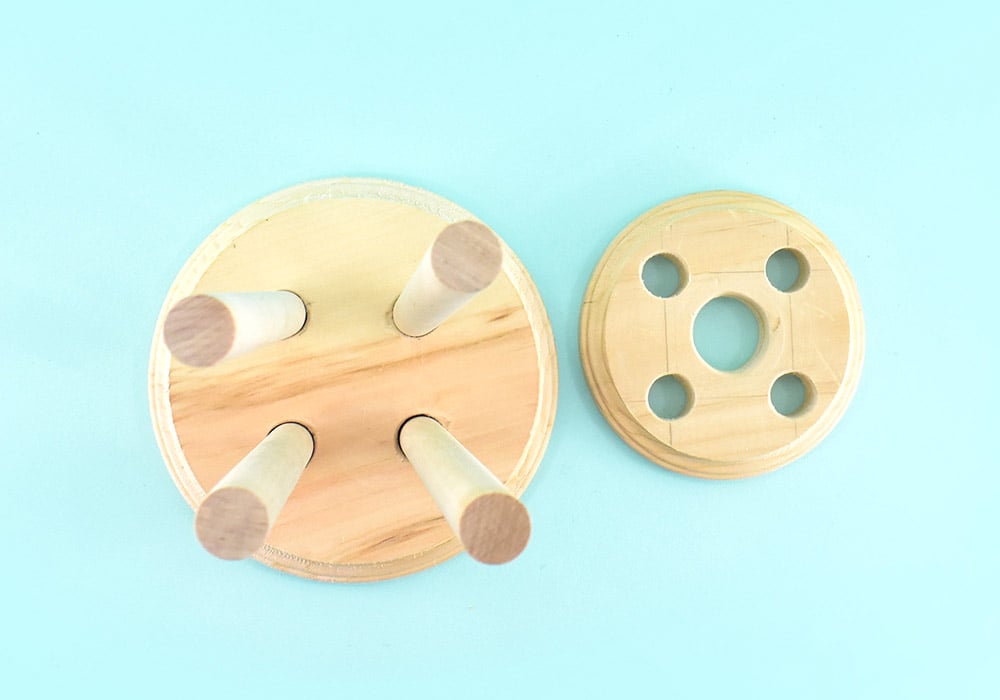 Flip your bottom round beveled side up on your work surface. Ensure that your wood dowels are the same length and trim, if necessary. Push a dowel into each of the leg holes on the bottom piece, making sure the bottoms are flush with the bottom of the plaque.